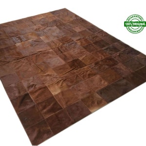 Puede incluir: Una alfombra de piel de vaca de color marrón con diseño de patchwork hecha de muchos cuadrados de cuero. La alfombra está hecha de piel de vaca natural y tiene un aspecto rústico y natural.