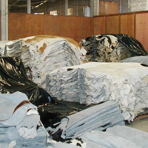 May include: A large warehouse space filled with stacks of tanned animal hides. The hides are stacked in various sizes and colors, including white, brown, and black.