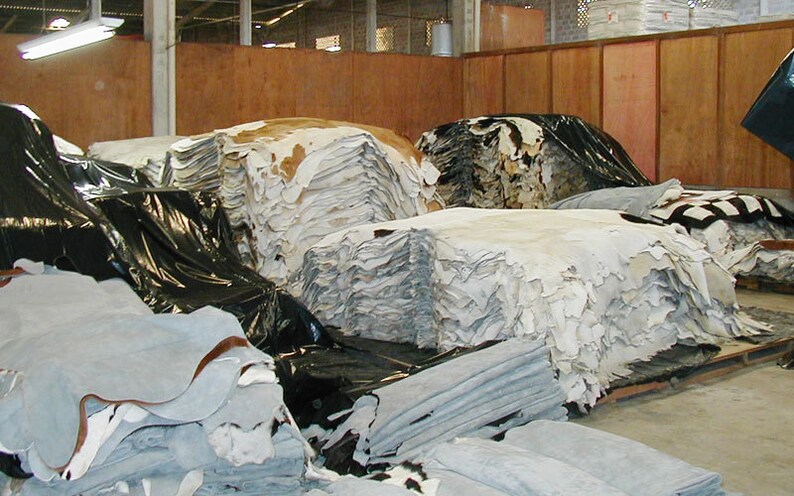 May include: A large warehouse space filled with stacks of tanned animal hides. The hides are stacked in various sizes and colors, including white, brown, and black.