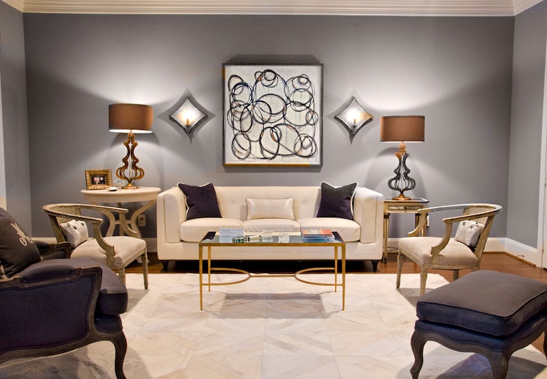 May include: A living room with a white sofa, two armchairs, a coffee table, and two lamps. The walls are painted a light gray, and the rug is a white cowhide. There is a large abstract painting on the wall above the sofa.