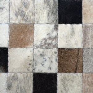 May include: A patchwork rug made of cowhide with a variety of brown, black, and white patterns.