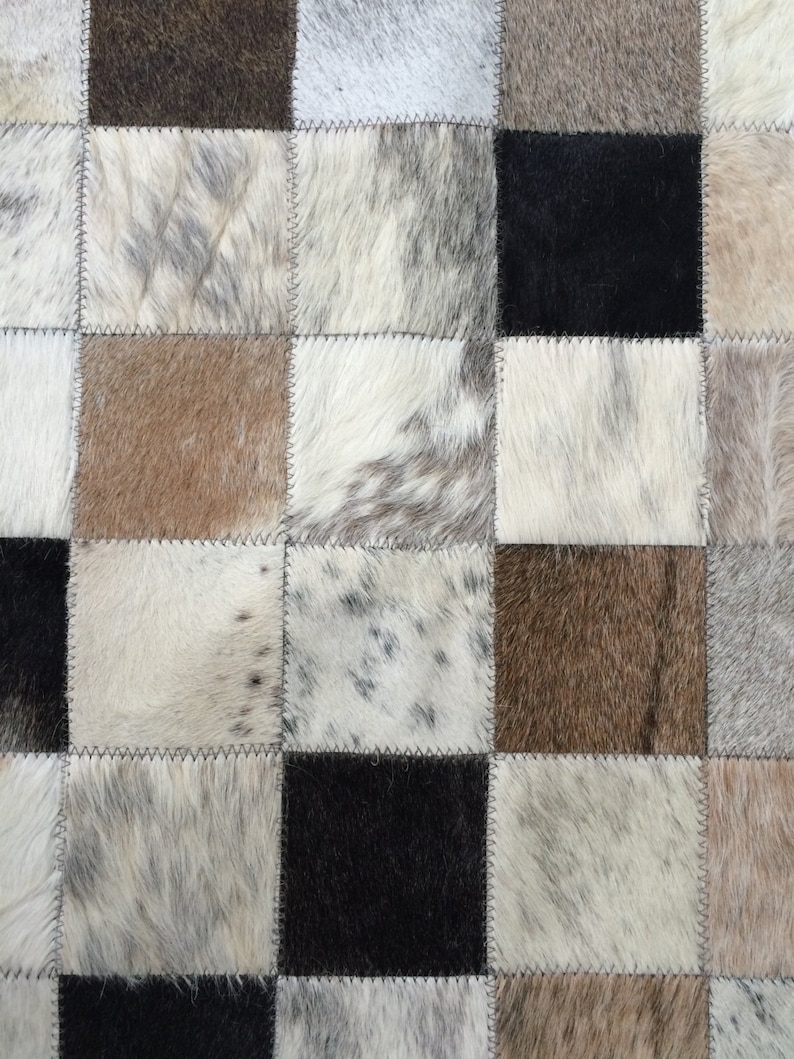 May include: A patchwork rug made of cowhide with a variety of brown, black, and white patterns.