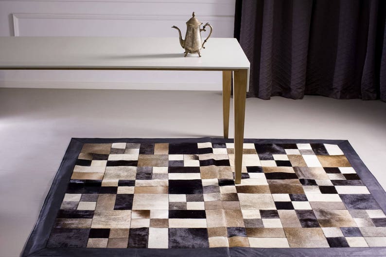 May include: A white table with a silver teapot on top, sitting on a black and white patchwork rug.