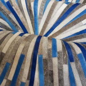 May include: A blue and gray patchwork rug made of cowhide. The rug is arranged in a circular pattern with the strips of leather radiating outward from the center.