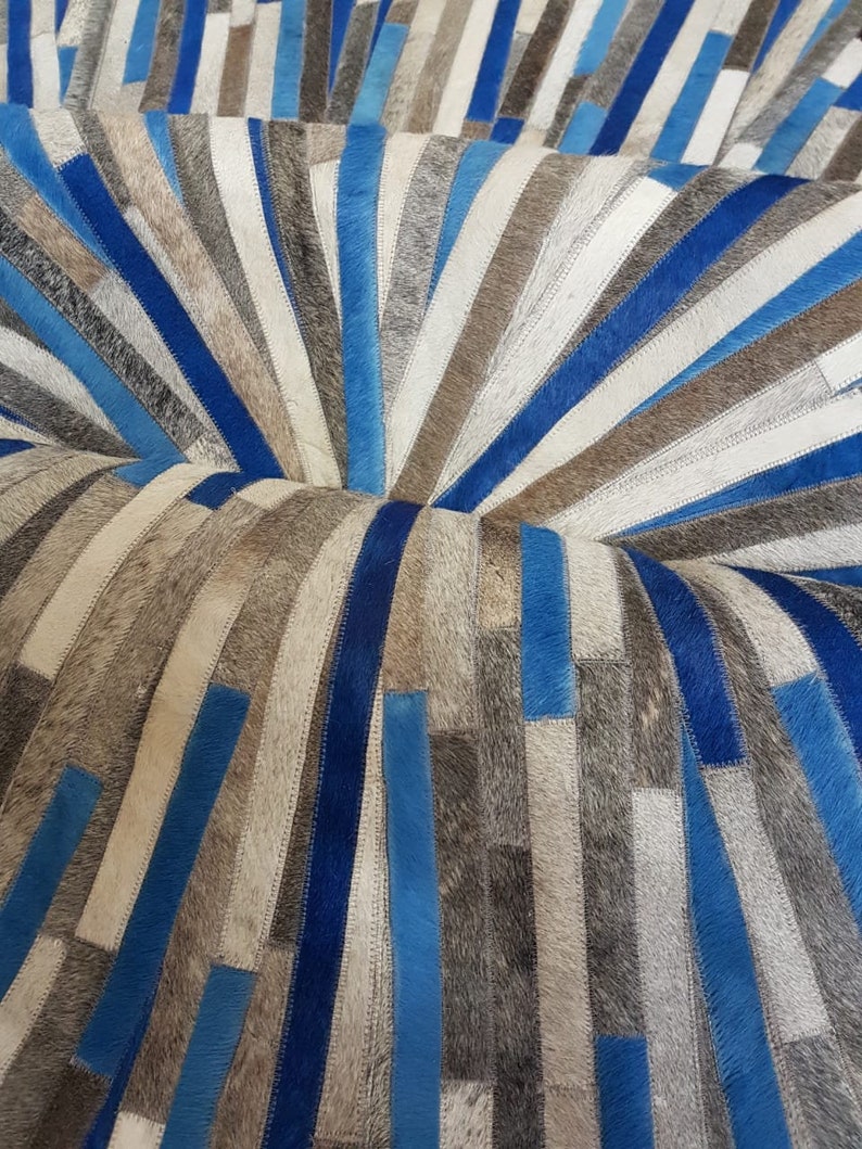 May include: A blue and gray patchwork rug made of cowhide. The rug is arranged in a circular pattern with the strips of leather radiating outward from the center.