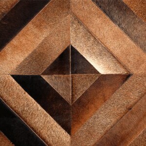 May include: A geometric patterned rug made of brown, black, and tan leather hides. The rug has a diamond shape with a smaller diamond in the center.