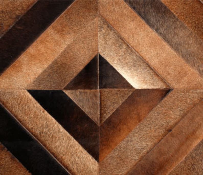 May include: A geometric patterned rug made of brown, black, and tan leather hides. The rug has a diamond shape with a smaller diamond in the center.