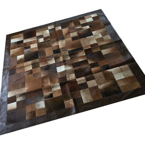 May include: A patchwork rug made of brown, tan, and white leather hides. The rug has a dark brown leather border.