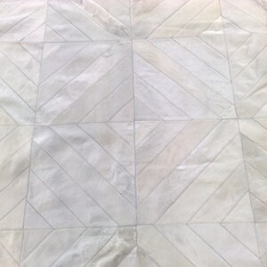 May include: White cowhide rug with a geometric pattern of diagonal stripes. The rug is made of natural leather and has a soft, luxurious feel.