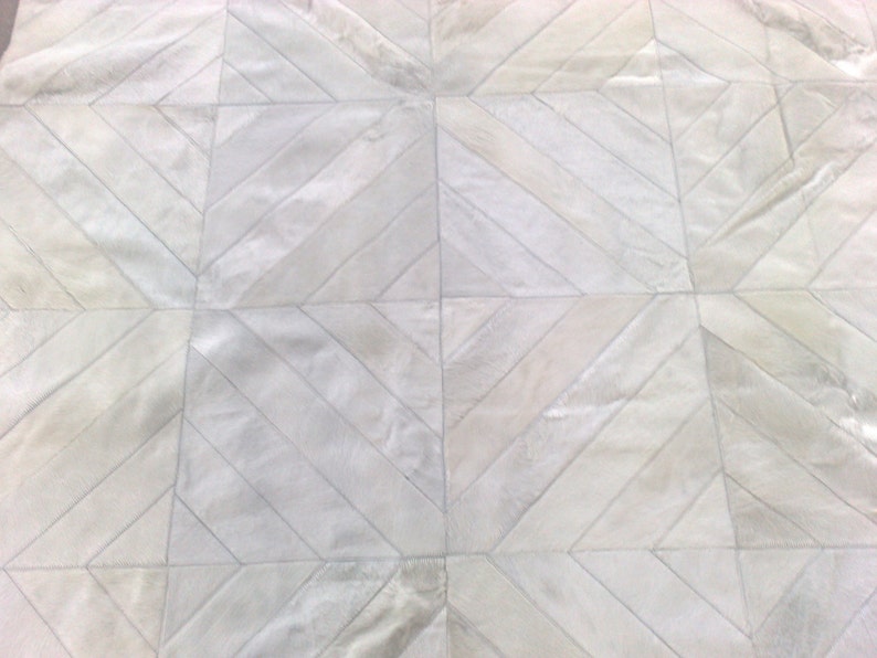May include: White cowhide rug with a geometric pattern of diagonal stripes. The rug is made of natural leather and has a soft, luxurious feel.