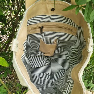 May include: A white cowhide tote bag with a tan leather lining. The bag has a zippered pocket and a small interior pocket. The lining is striped in black and white.