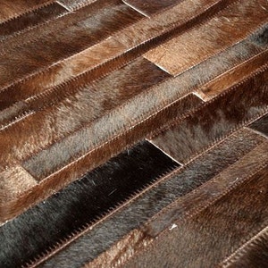 May include: A brown and black cowhide rug with a patchwork design. The rug is made of strips of cowhide sewn together to create a geometric pattern.