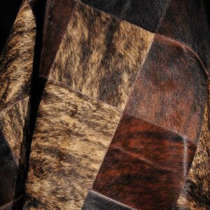 May include: A patchwork cowhide rug with squares of brown, black, and tan cowhide. The rug is made of natural leather and has a soft, luxurious feel.