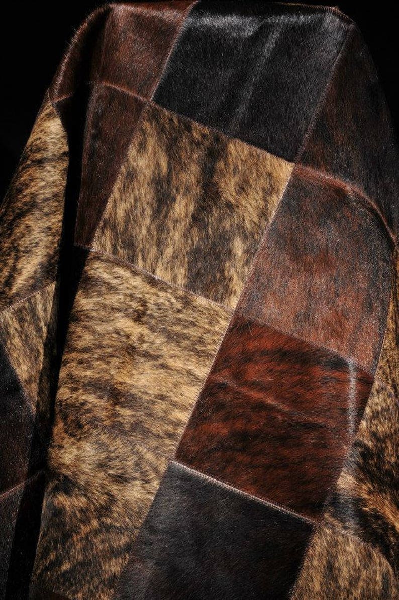 May include: A patchwork cowhide rug with squares of brown, black, and tan cowhide. The rug is made of natural leather and has a soft, luxurious feel.