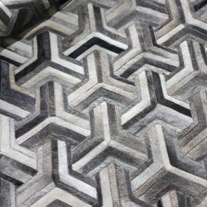 May include: A geometric patterned rug made from cowhide in shades of grey and white.