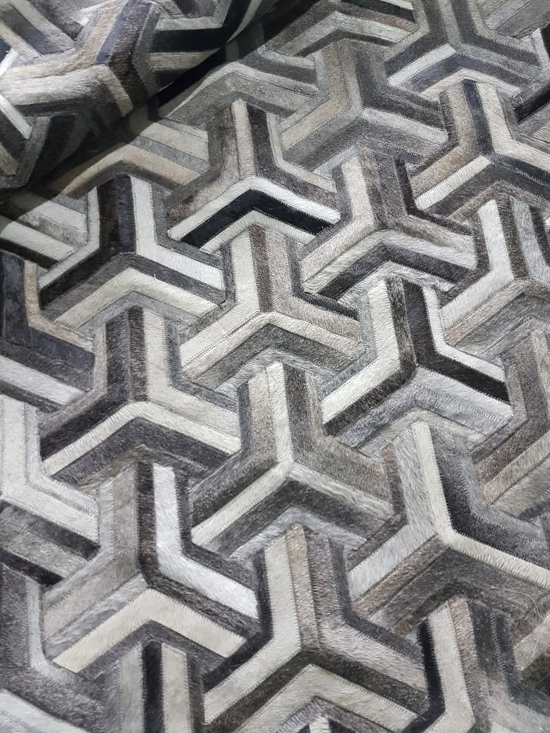 May include: A geometric patterned rug made from cowhide in shades of grey and white.