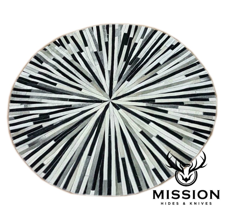 May include: A round, black and white cowhide rug with a radial pattern. The rug is made of strips of leather sewn together to create a sunburst design. The rug is approximately 3 feet in diameter.
