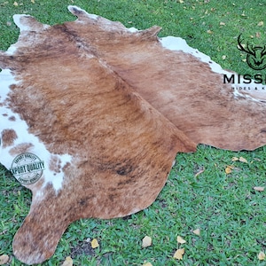 May include: Brown and white cowhide rug with an "Export Quality" stamp. The rug is laid out on a green grassy surface.