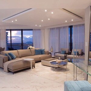 May include: A modern living room featuring a large sectional sofa, a glass coffee table, and a view of the city skyline. The room is decorated in a neutral colour palette with pops of blue.