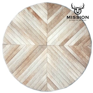 May include: A round, cream-colored cowhide rug with a geometric pattern of brown and white stripes. The rug is made of leather and has a soft, luxurious feel. The rug is perfect for adding a touch of rustic elegance to any room.