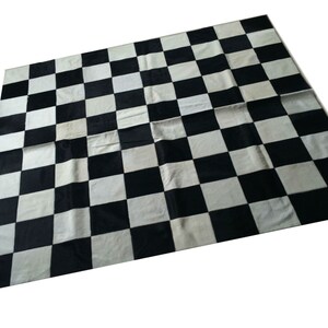 Puede incluir: Alfombra a cuadros en blanco y negro hecha de piel de vaca. La alfombra está hecha de cuadrados de piel de vaca blanca y negra.