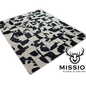May include: Black and white cowhide patchwork rug. The rug is made of squares of cowhide, with some squares being black and some being white. The rug is a checkerboard pattern. The rug is made by Mission Hides & Knives.