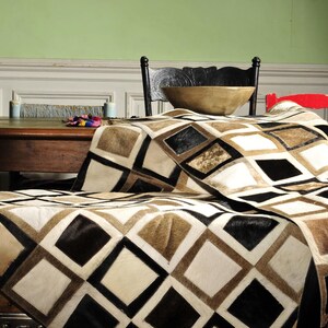 May include: A brown, black, and white patchwork cowhide rug with a diamond pattern. The rug is draped over a wooden table and chair.