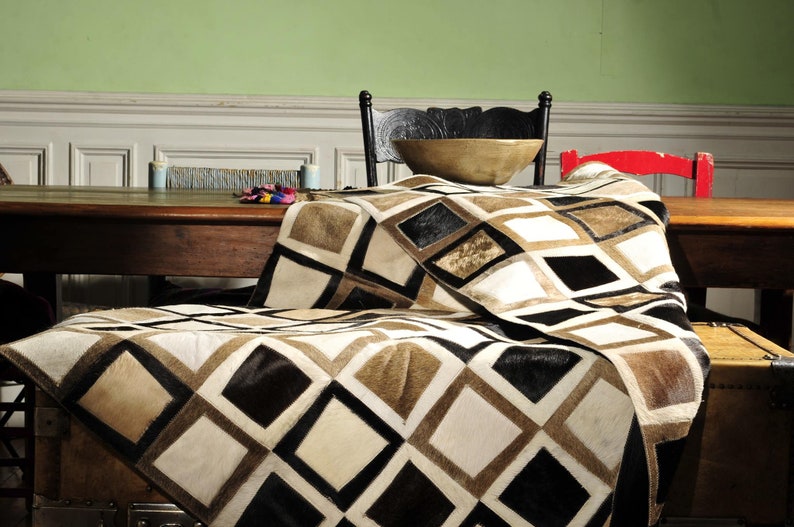 May include: A brown, black, and white patchwork cowhide rug with a diamond pattern. The rug is draped over a wooden table and chair.