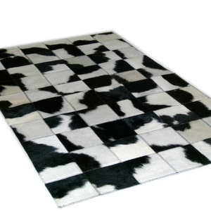 May include: Black and white cowhide rug with a checkered pattern. The rug is made of individual pieces of cowhide that have been sewn together.