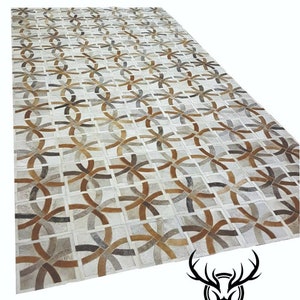 May include: A geometric patterned rug made from leather in shades of brown, gray, and white. The rug is made up of individual pieces of leather that are sewn together to create a unique design.