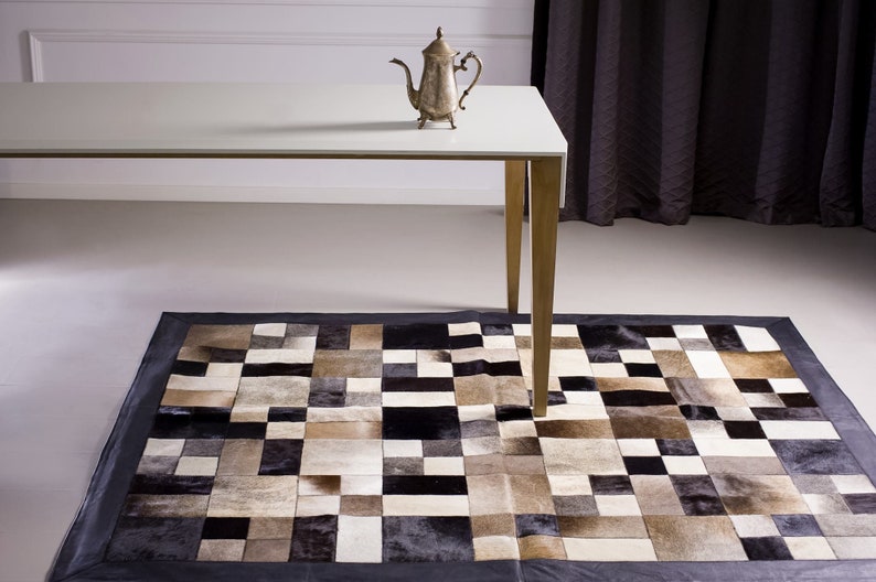 May include: A white table with a silver teapot on top, sitting on a black and white patchwork rug.