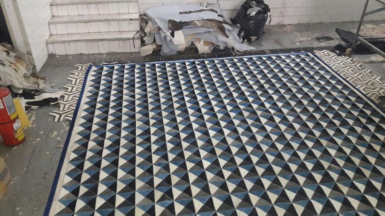 May include: A black and white geometric rug with a pattern of triangles. The rug has a blue border and is made of a soft, durable material.