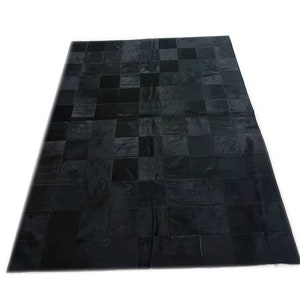 May include: Black patchwork cowhide rug with a square pattern. The rug is made of different pieces of leather sewn together.