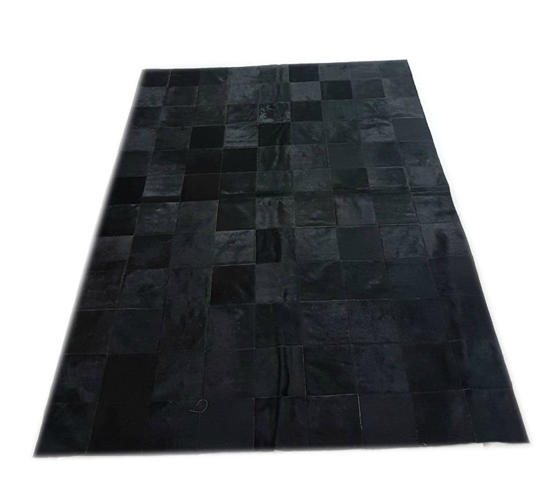 May include: Black patchwork cowhide rug with a square pattern. The rug is made of different pieces of leather sewn together.
