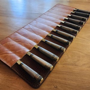 May include: A brown leather roll with 12 slots for holding knives. The roll is closed and the knives are visible inside.