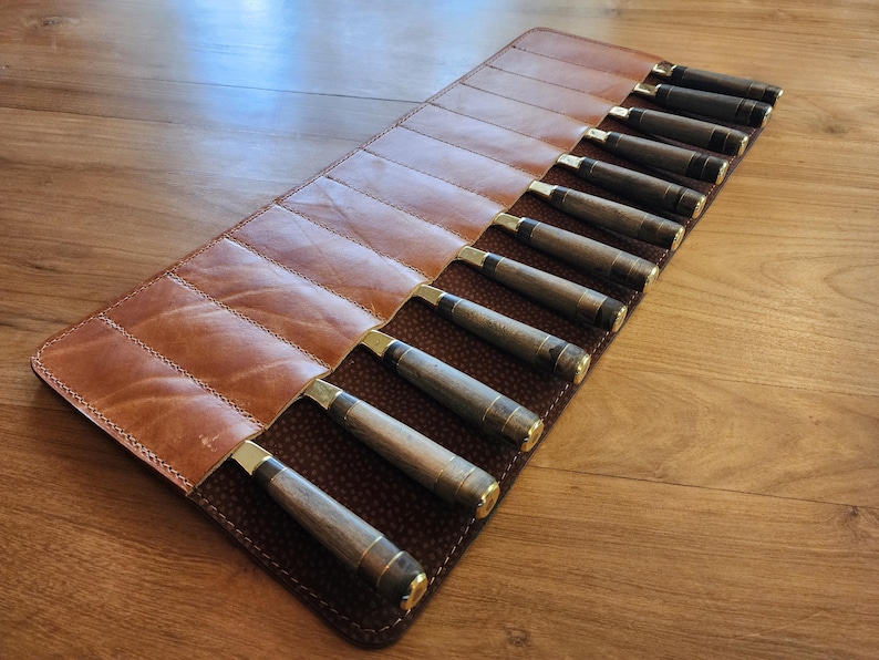 May include: A brown leather roll with 12 slots for holding knives. The roll is closed and the knives are visible inside.