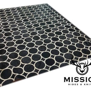 Puede incluir: Alfombra de piel de vaca negra y blanca con un patrón geométrico de círculos. La alfombra está hecha de cuero genuino y tiene una sensación suave y lujosa.
