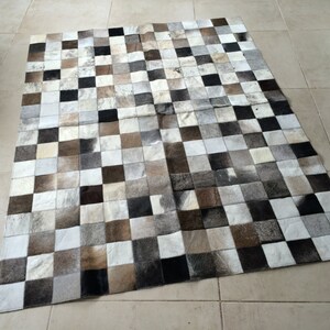 May include: A checkered patchwork rug made of cowhide in shades of white, brown, and black.