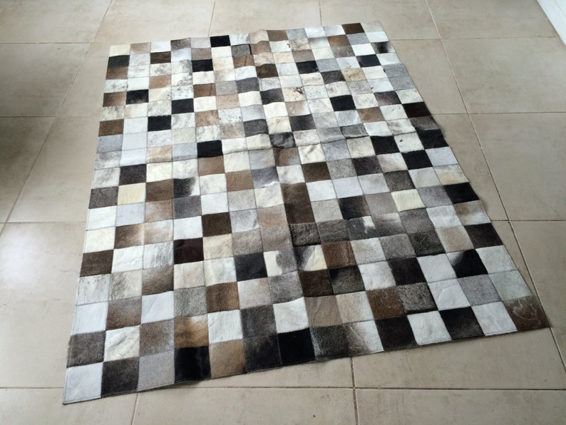 May include: A checkered patchwork rug made of cowhide in shades of white, brown, and black.