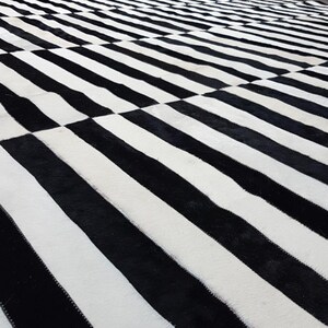 Puede incluir: Alfombra rayada en blanco y negro hecha de piel de vaca. La alfombra tiene un patrón geométrico con rayas blancas y negras alternas.