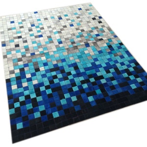 May include: A blue and grey patchwork rug made of leather squares. The rug has a gradient pattern, starting with light grey squares at the top and transitioning to dark blue squares at the bottom.