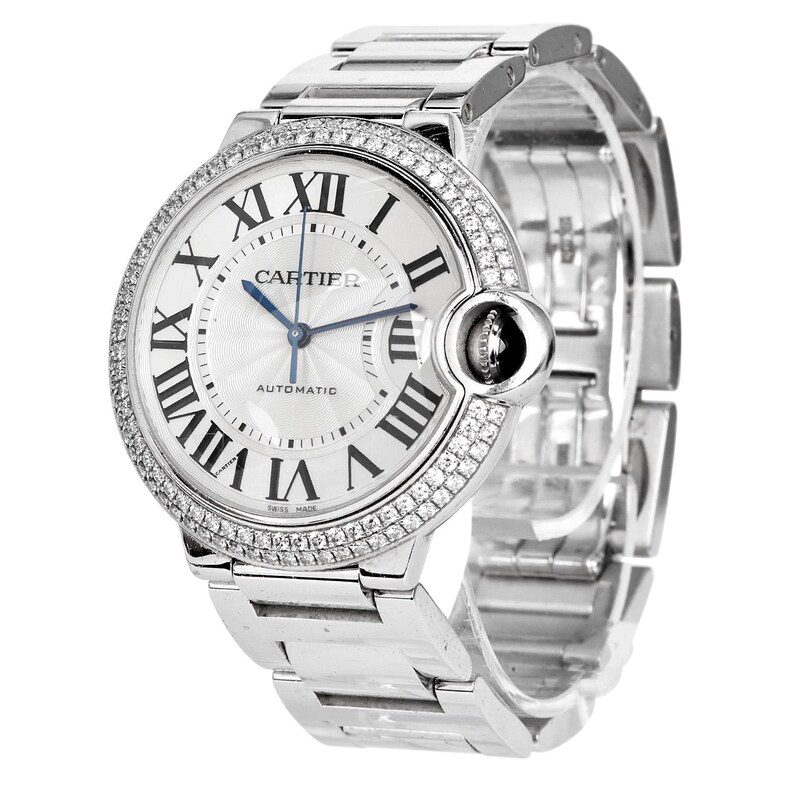 Puede incluir: Un reloj Cartier Ballon Bleu de Cartier plateado con un bisel engastado con diamantes y una esfera blanca. El reloj presenta marcadores de hora en n&uacute;meros romanos, una aguja de acero azul y una ventana de fecha a las 3 en punto. El reloj es autom&aacute;tico y tiene un cristal de zafiro.