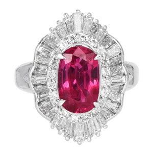 Puede incluir: Un anillo de plata con una gran gema roja rubí de corte ovalado en el centro. La gema está rodeada por un halo de diamantes más pequeños y transparentes con corte baguette y un diseño festoneado. La banda del anillo es lisa y pulida.