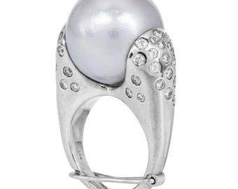 Pode incluir: Um anel de prata com uma grande pérola redonda cinza engastada no centro. O anel é adornado com pequenos diamantes transparentes em torno da pérola e na banda.