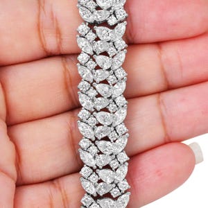 May include: A dazzling diamond bracelet featuring a repeating pattern of marquise and round-cut stones. The bracelet is set in a silver-toned metal and is held in a hand, showcasing its intricate design and brilliant sparkle.