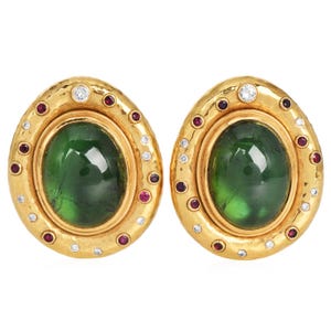 May include: A pair of gold oval earrings with green gemstones surrounded by a halo of smaller diamonds and rubies.