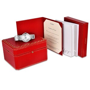Puede incluir: Un reloj Cartier plateado con esfera blanca y detalles de diamantes viene en una caja roja con un certificado de origen. La caja est&aacute; forrada con ribetes dorados.