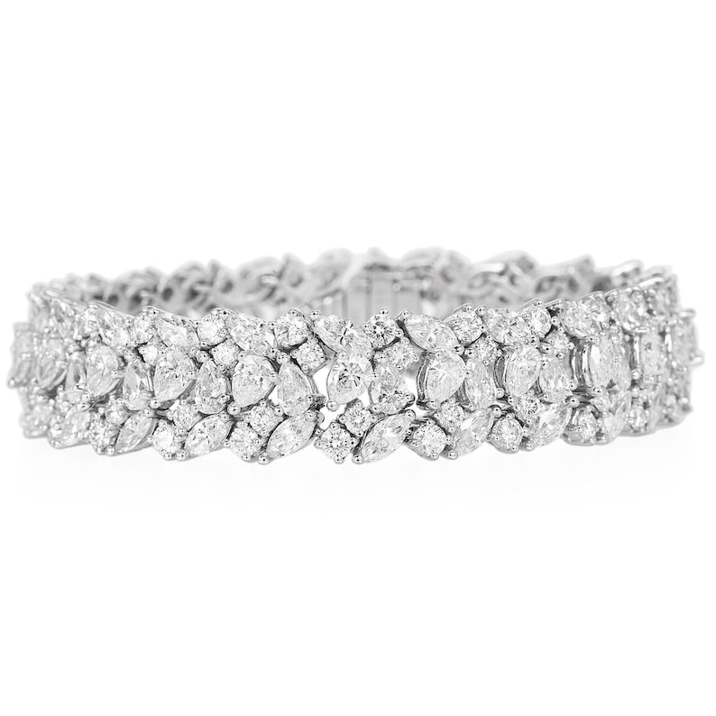 May include: A dazzling, silver-toned bracelet featuring a double-row design. The bracelet is adorned with numerous clear, sparkling gemstones in various shapes, including marquise and round cuts. The overall design is symmetrical and elegant.