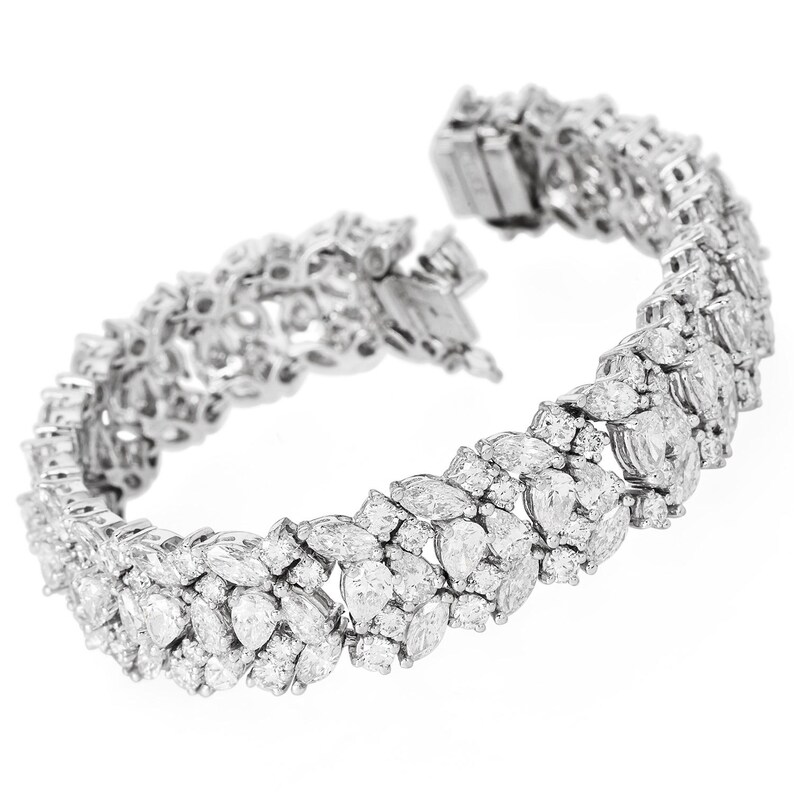 May include: A dazzling white gold bracelet, encrusted with numerous clear, sparkling diamonds. The bracelet features a variety of diamond cuts, including marquise and round shapes, set closely together. The clasp is visible at the top.