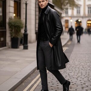 May include: A black leather trench coat with a matching black turtleneck and dark gray trousers. The coat is knee-length and has a classic design. The outfit is completed with black leather shoes. The person is walking on a cobblestone street.